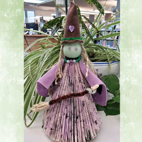 Witch made of folded book pages, with a felt hat, twine broom, and other crafting accessories