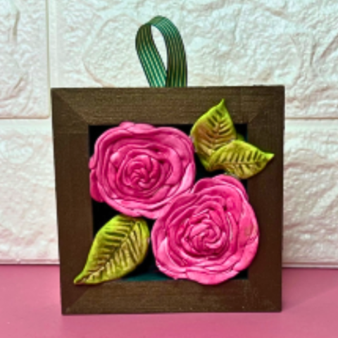 Two pink clay roses with a wooden frame