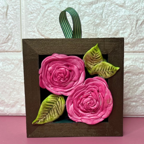 Two pink clay roses in a wooden frame