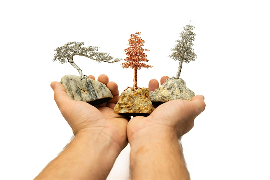 Pair of hands holding three wire tree sculptures anchored to fist-sized rocks