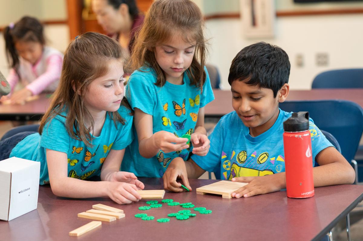 Three kids working together to build with wood pieces and plastic connectors.