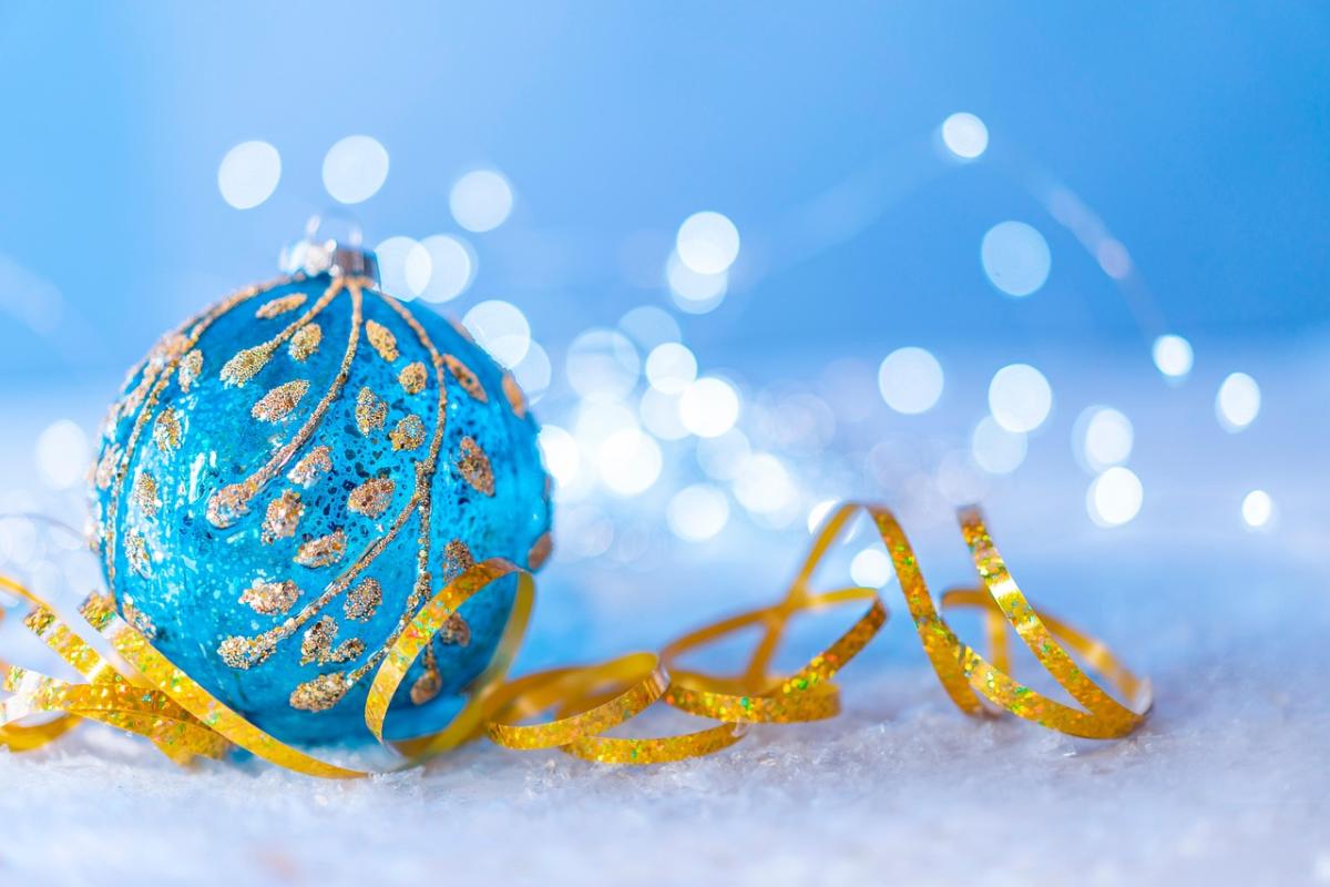 Sparkly blue ornament sitting on a gold ribbon and snow.