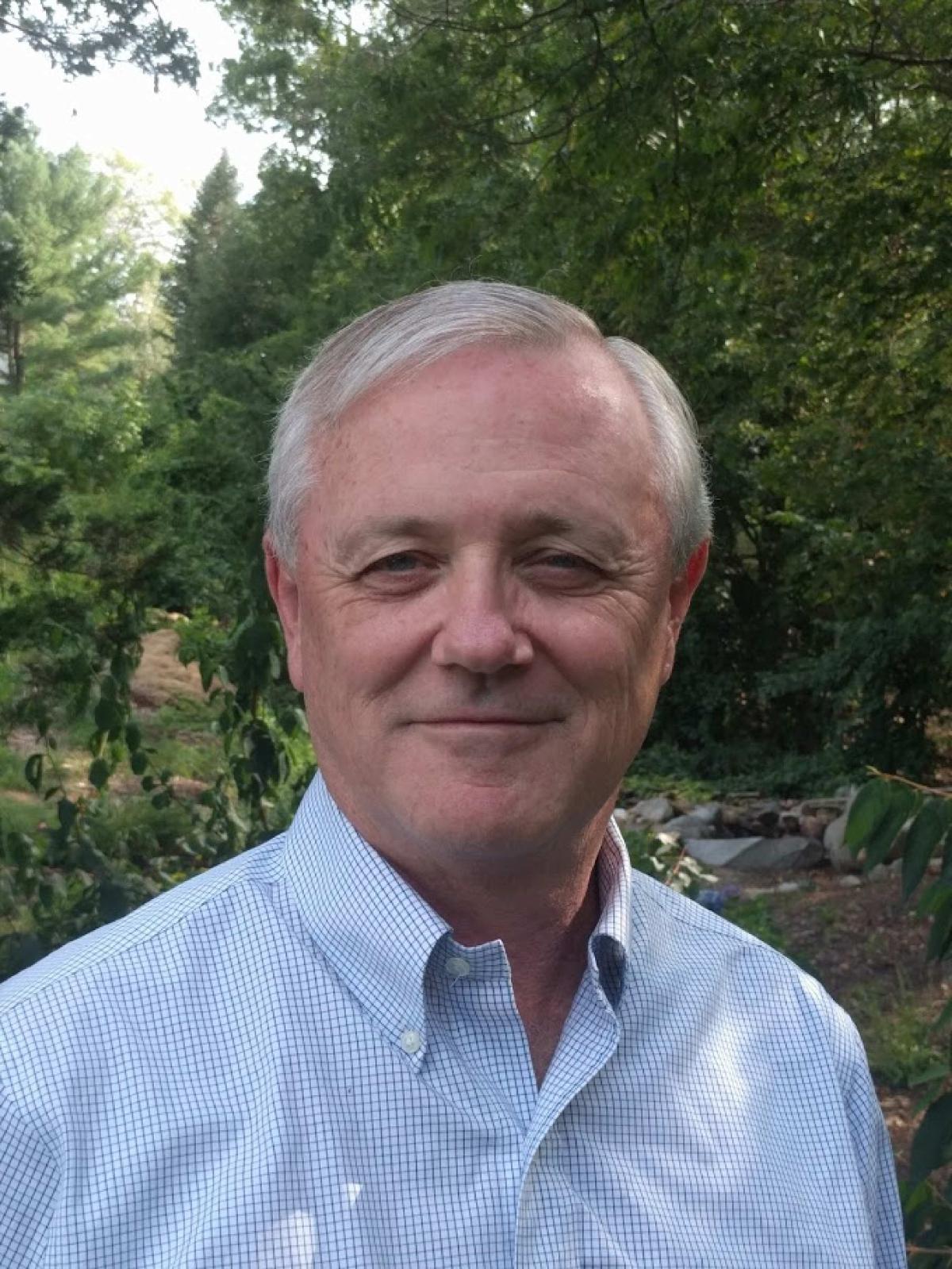 man in blue shirt standing in front of trees